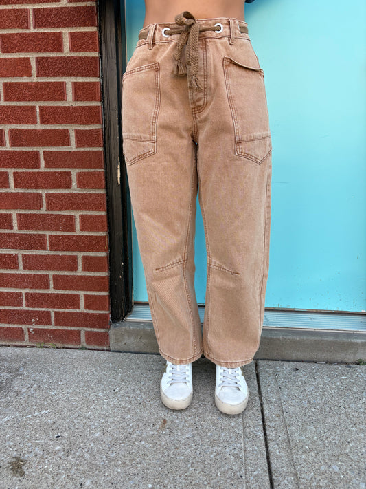Person wearing beige pants and white sneakers standing on a sidewalk with a blue wall in the background.