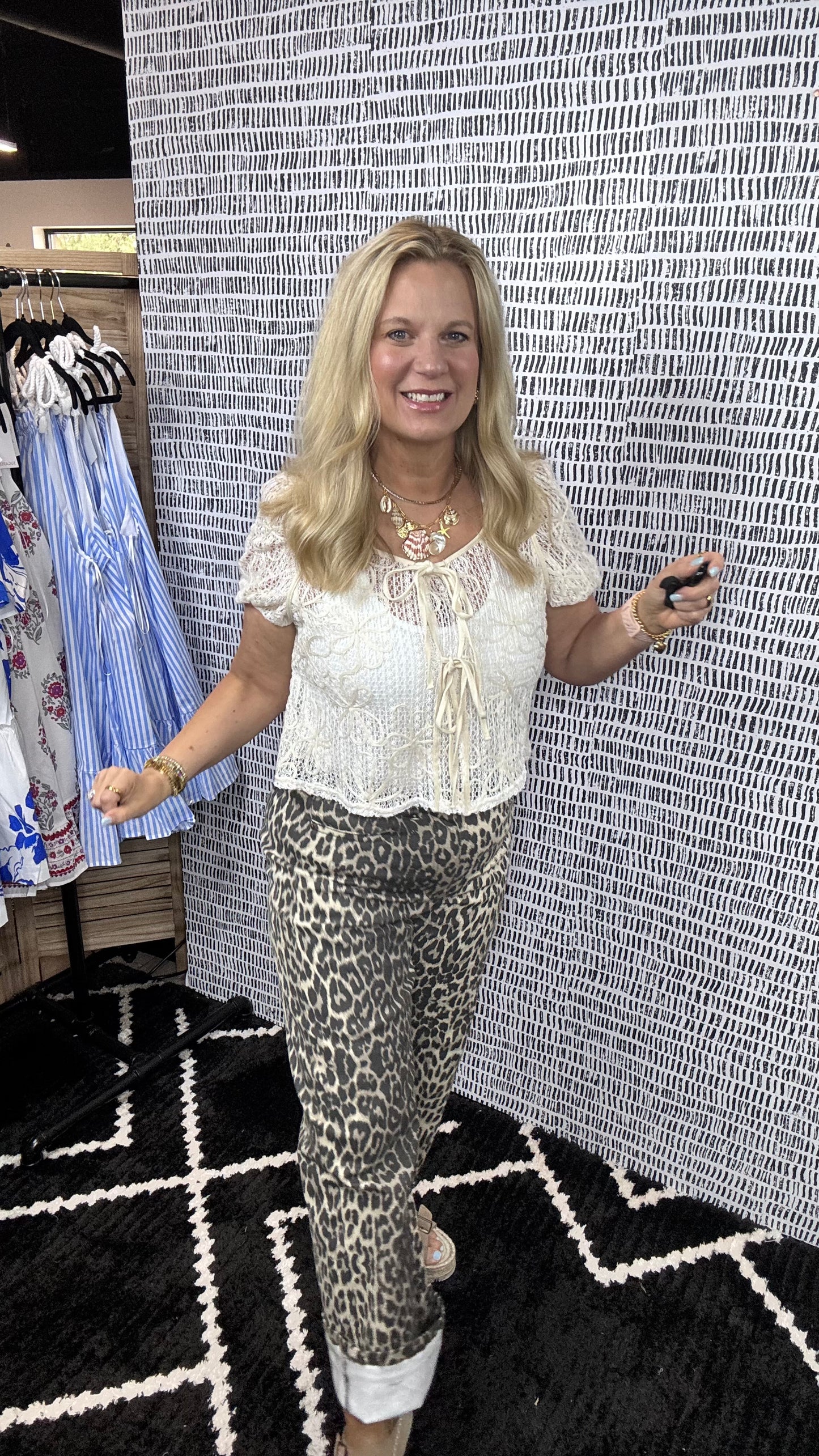 Woman in a white blouse and patterned pants standing in front of a textured wall.