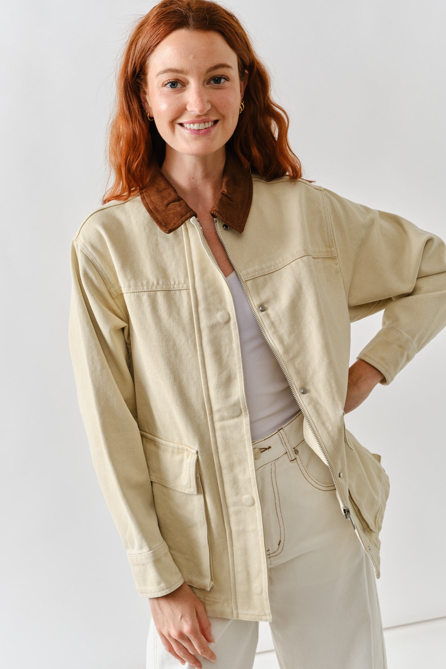 Woman wearing a beige utility barn jacket with brown corduroy collar, front pockets, and zip-up closure.