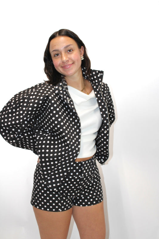 Black and white polka dot cropped jacket with zip front and structured collar styled with matching shorts.