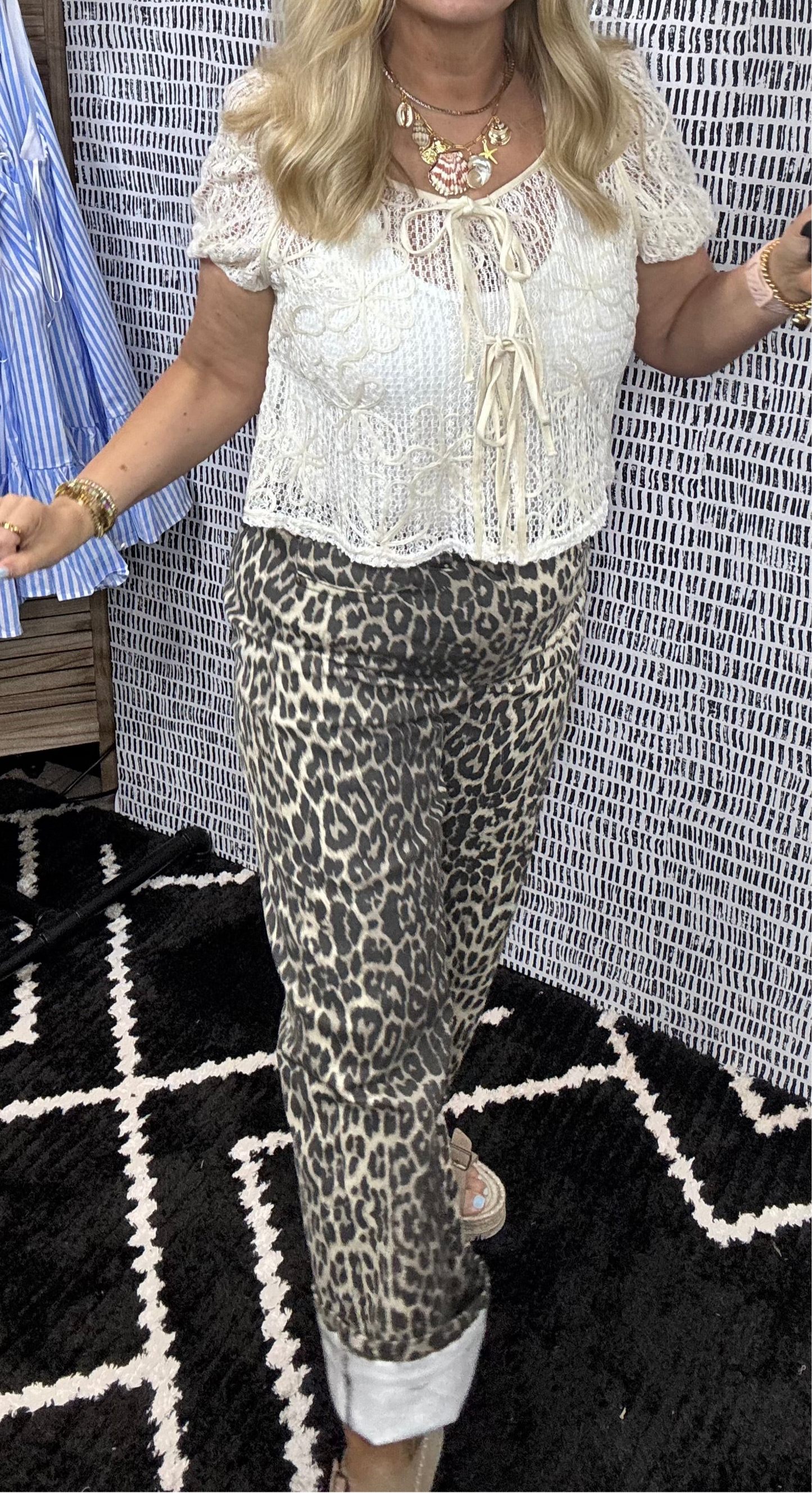 Person wearing a white lace top and leopard print pants in a store setting.