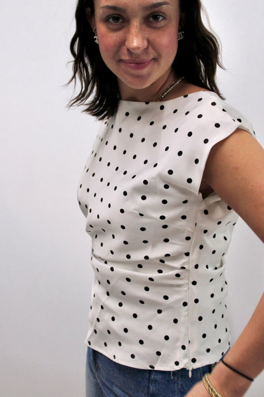 Cream sleeveless top with black polka dots and structured silhouette styled with denim.
