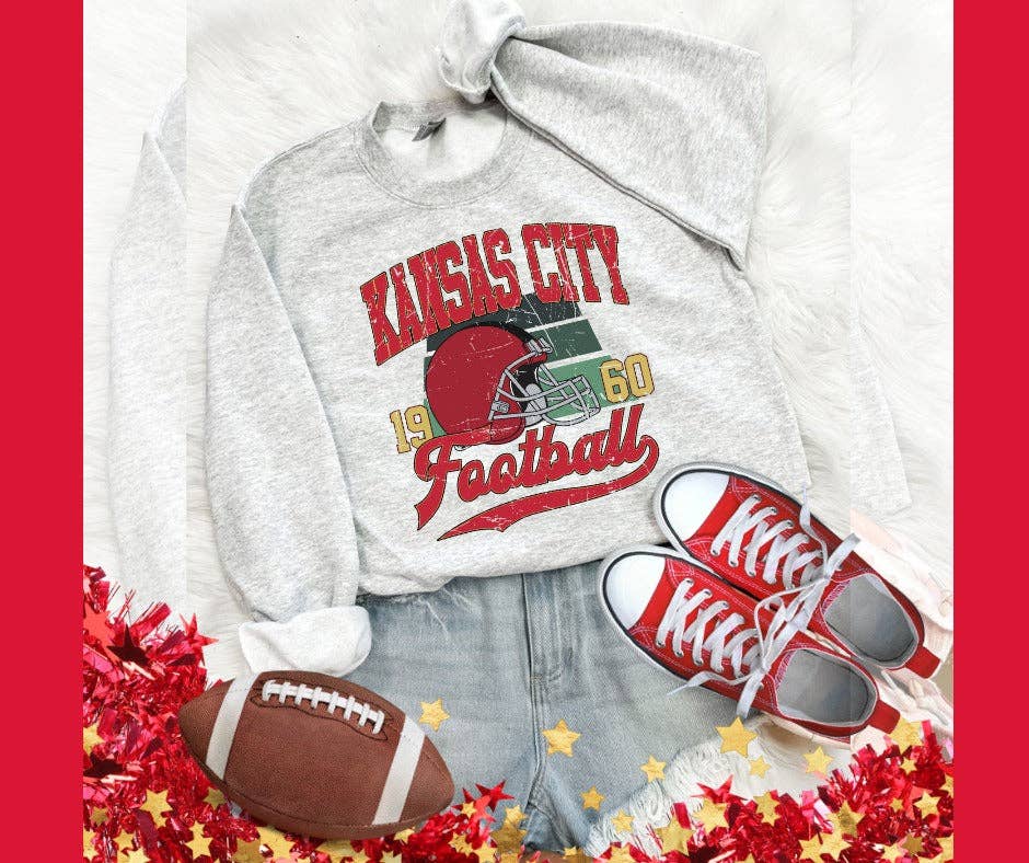 A vintage gray sweatshirt with 'KANSAS CITY 1960 FOOTBALL' text and a graphic design, accompanied by a pair of red and white sneakers and a football.