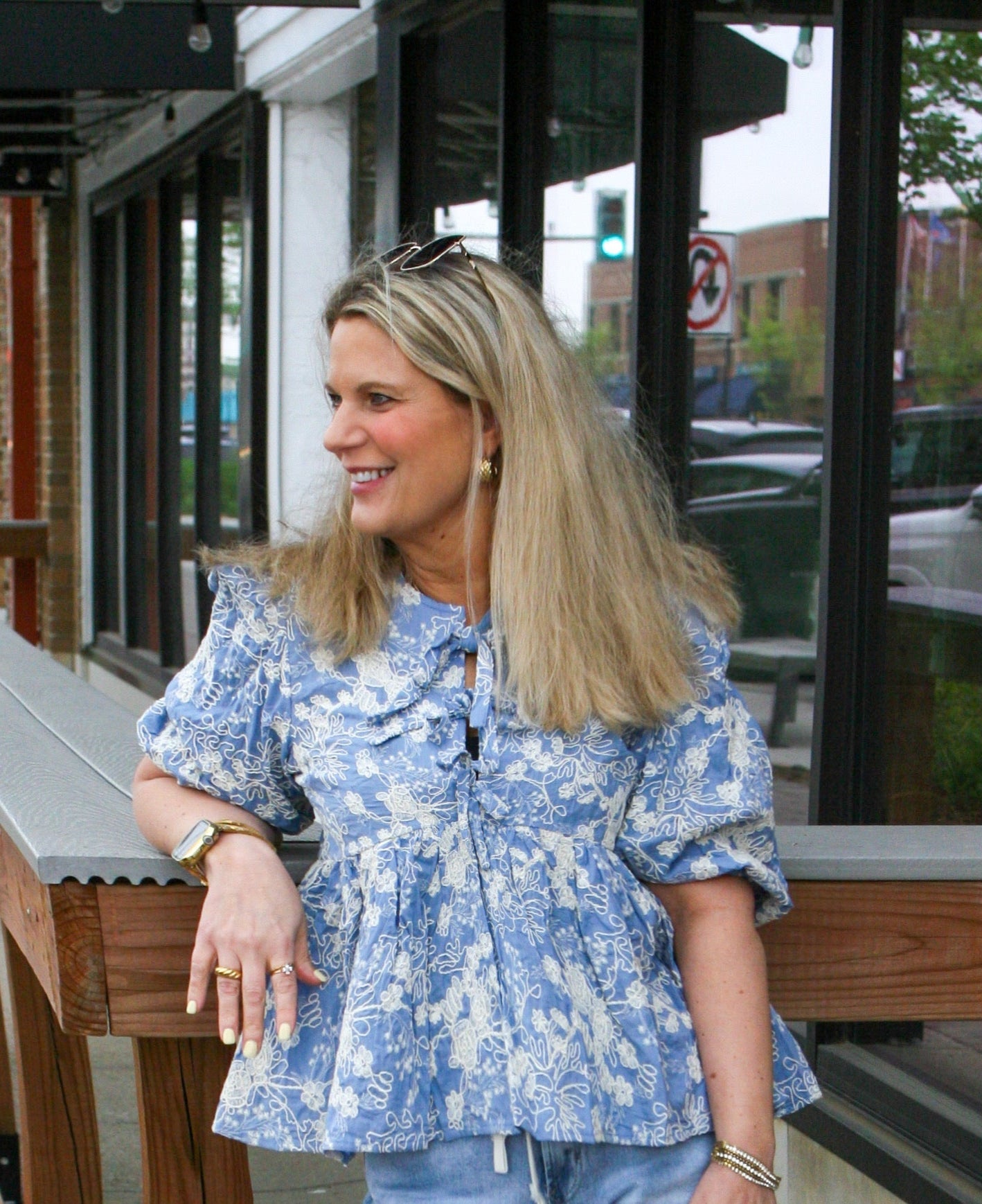 Woman standing outside wearing a light blue puff sleeve blouse with ivory floral embroidery and bow front ties – styled spring outfit with boutique top