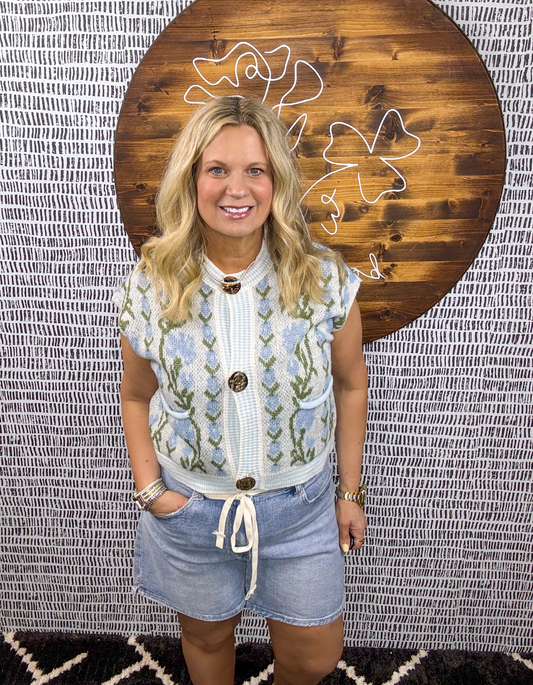 Woman wearing blue and white floral knit vest with floral detail, paired with drawstring denim shorts, styled at Erin Rose Boutique