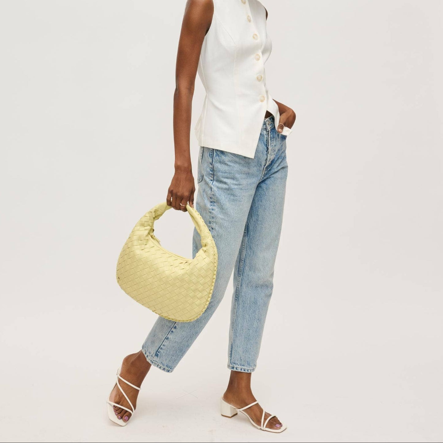 Model carrying butter yellow woven hobo bag, styled with white sleeveless button top, light wash jeans, and white strappy heels – Erin Rose Boutique