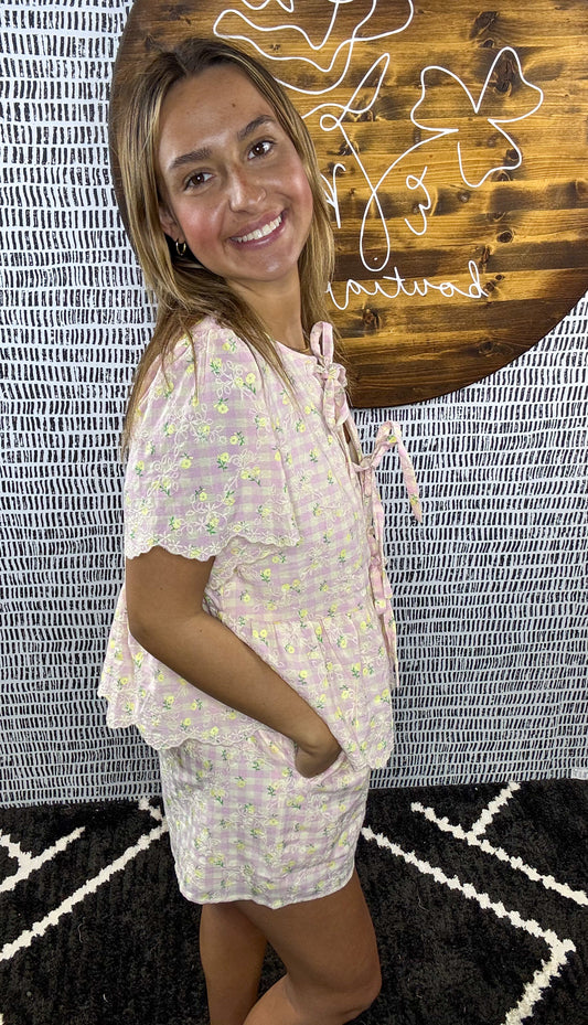 Side view of woman wearing pastel pink floral gingham two-piece summer set with tie front top and shorts, boutique outfit for women