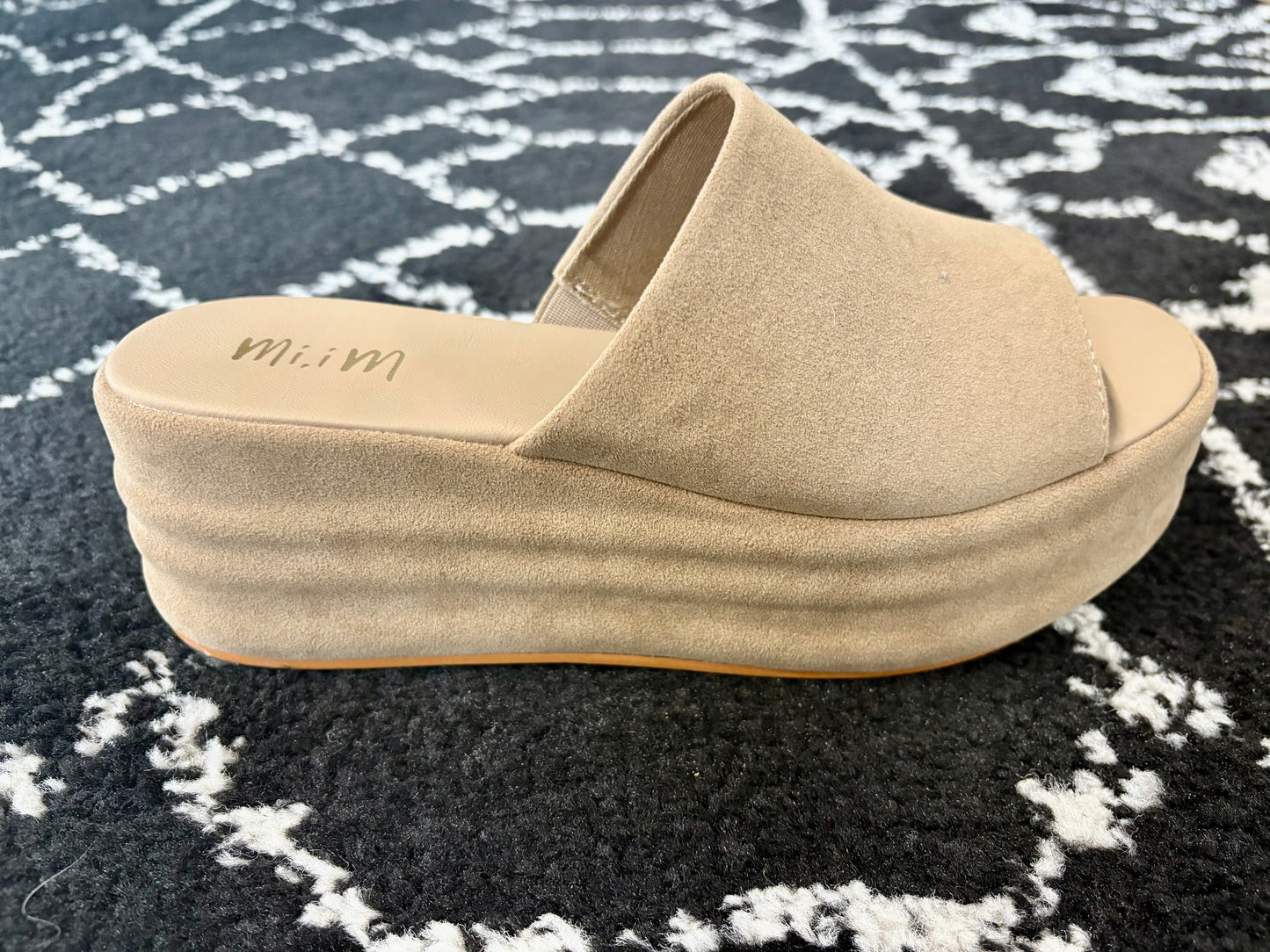 Side view of the Hazel Platform Slide sandal in tan faux suede with a thick platform sole, displayed on a black and white rug.