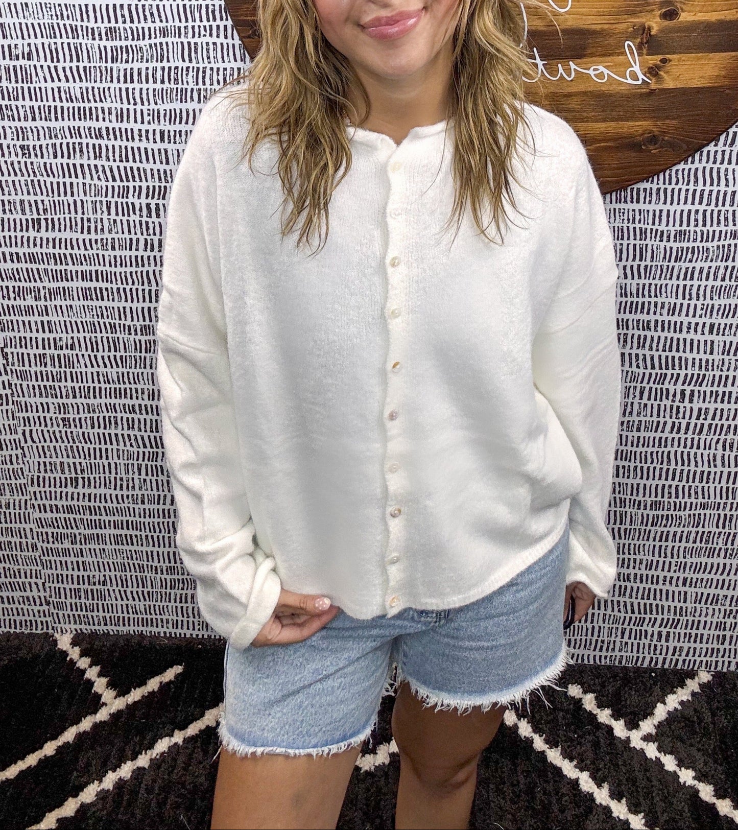 Woman wearing an ivory button-up cardigan paired with high-rise light wash denim shorts – casual and comfy summer outfit for women