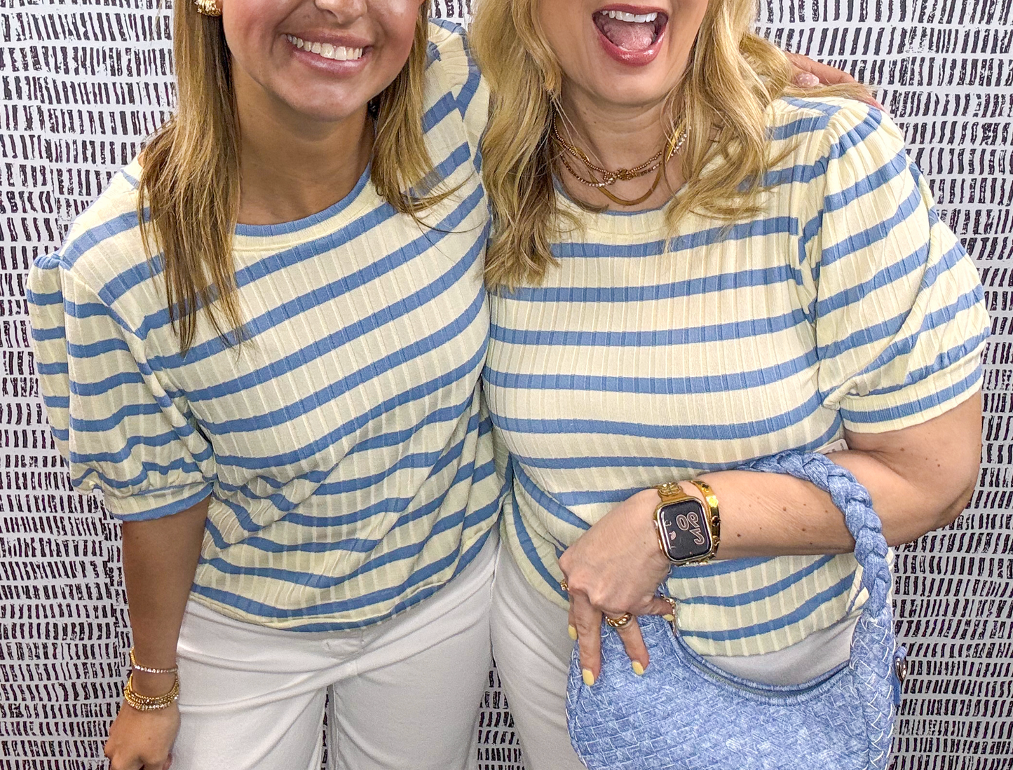 Two women smiling and wearing yellow and blue pastel striped puff sleeve tops with white pants – cheerful spring or summer boutique outfit inspiration