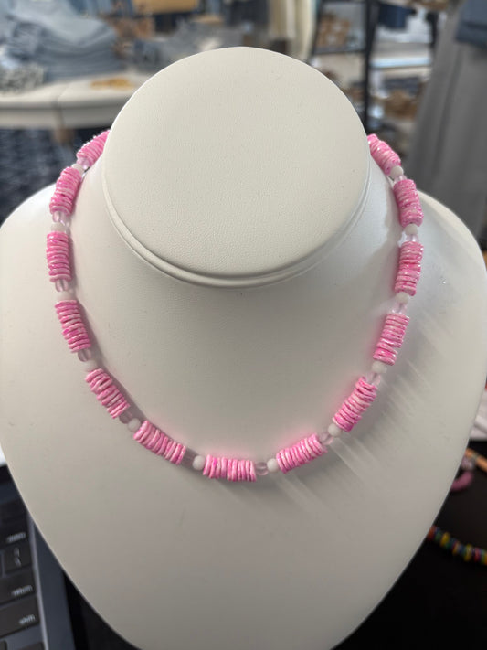 Pink puka shell necklace with white spacer beads displayed on a white bust stand, boutique summer jewelry
