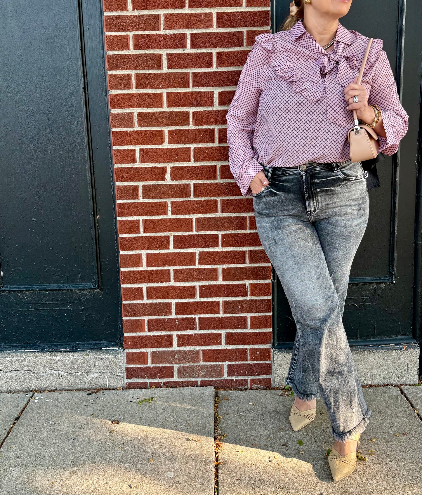Person wearing a pink and black polka dot blouse with ruffles and jeans standing against a brick wall.
