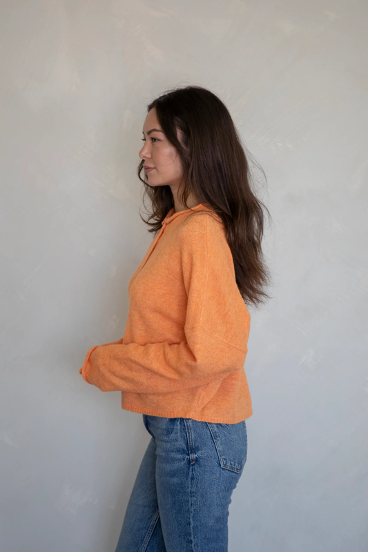 Woman wearing an orange cardigan sweater and blue jeans against a plain background