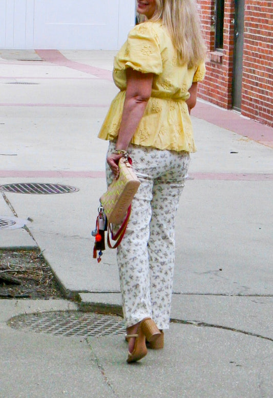 Back view of model wearing yellow embroidered puff sleeve top and white floral print pants, holding a clutch handbag – Erin Rose Boutique