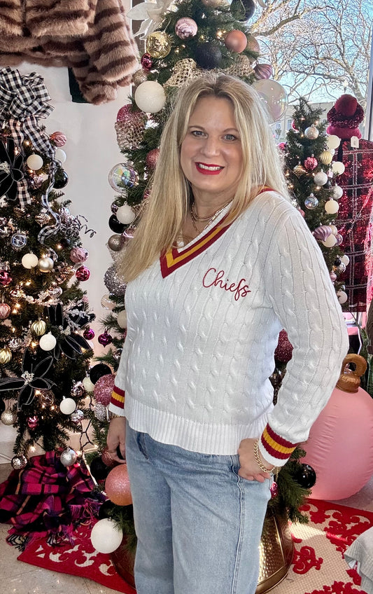 Woman wearing a white sweater with 'Cheifs' text in a festive setting with Christmas trees.