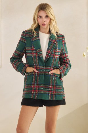 Woman wearing a green plaid blazer with a white top and black shorts on a beige background