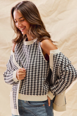 Woman wearing a houndstooth patterned sweater with cut-out shoulders against a beige background
