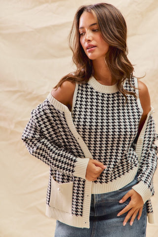 Woman wearing a black and white houndstooth patterned sweater with cut-out shoulders against a beige background.