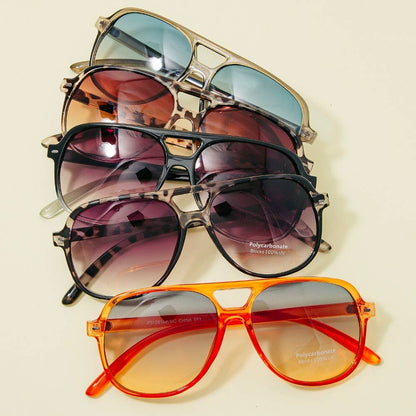 Stack of retro-inspired aviator sunglasses with polycarbonate frames in vibrant and neutral tones including orange, tortoiseshell, black, and clear, each with UV-blocking tinted lenses.