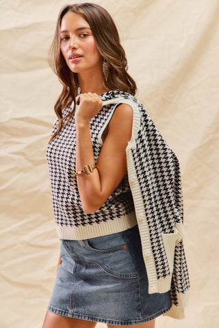 Woman wearing a houndstooth patterned cardigan over a sleeveless top with denim shorts against a beige background