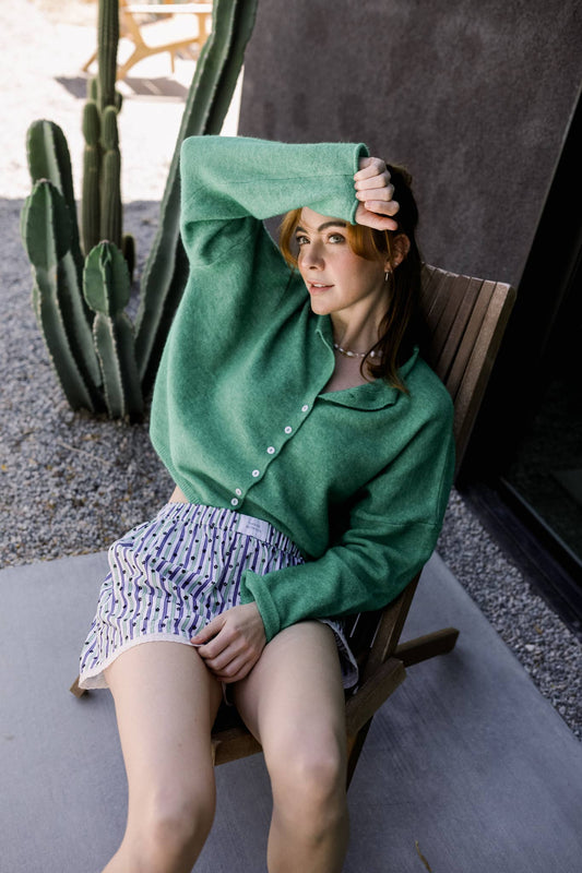 Model lounging outdoors in a green Coco Cutie Cardi, styled with striped shorts and surrounded by desert cactus vibes