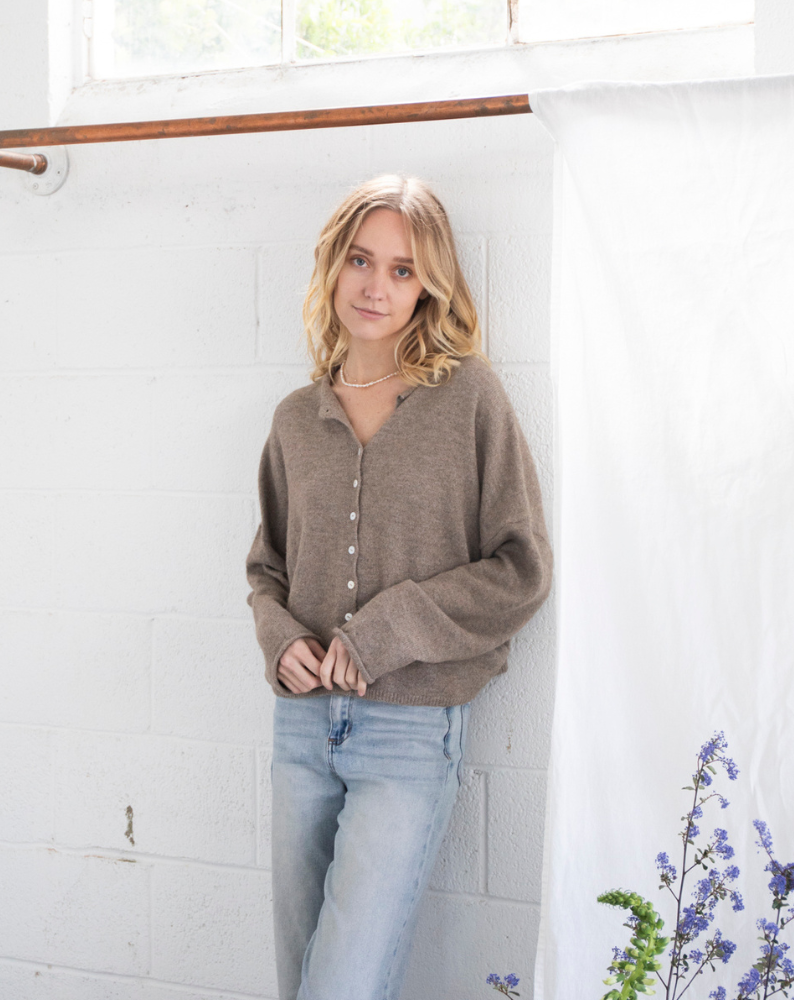 Model wearing the Coco Cutie Cardi, a soft brown button-up sweater, paired with light-wash jeans in a minimal studio setting