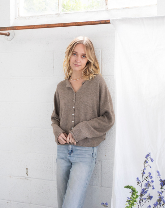 Model wearing the Coco Cutie Cardi, a soft brown button-up sweater, paired with light-wash jeans in a minimal studio setting