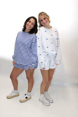 Two women wearing matching outfits with blue and white stripes on a white background