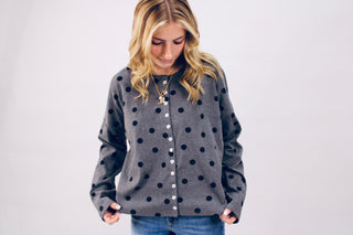 Woman wearing a gray cardigan with black polka dots on a white background