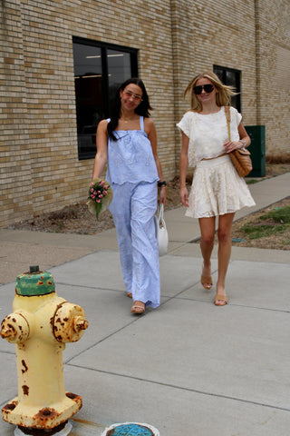 Two women walking on a sidewalk next to a fire hydrant with a brick building in the background.