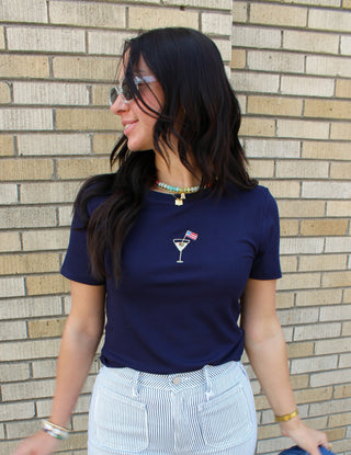 Woman wearing a navy blue t-shirt with a cocktail graphic in front of a brick wall.