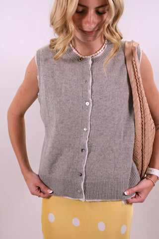 Woman wearing a gray sleeveless cardigan over a yellow dress with a white polka dot pattern.