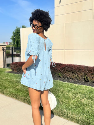 Back view of women’s light wash denim romper with delicate floral embroidery