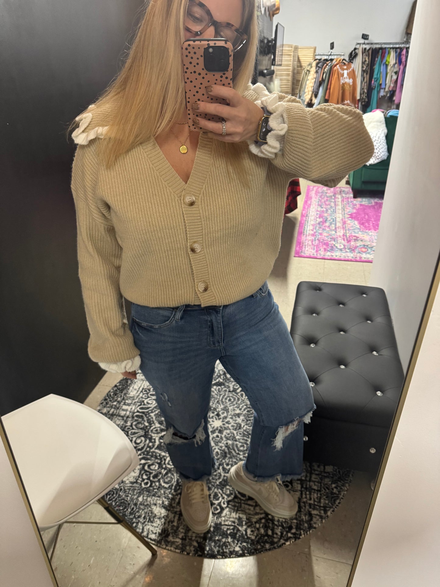 Woman wearing a beige cardigan sweater with ruffle shoulder details, button front, and ribbed knit texture, paired with distressed jeans available at Erin Rose Boutique.