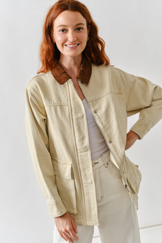 Woman wearing a beige utility barn jacket with brown corduroy collar, front pockets, and zip-up closure.