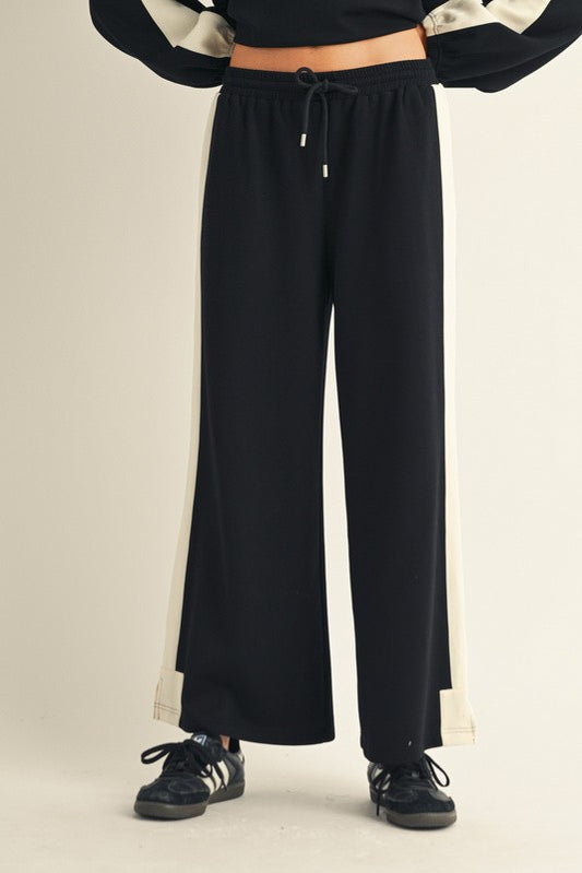 Woman wearing black wide leg pants with ivory side stripes and a drawstring waist.