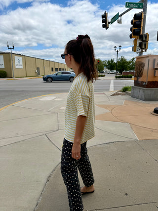 Women's butter yellow and white striped oversized tee styled with black polka dot pants and casual flip flops.