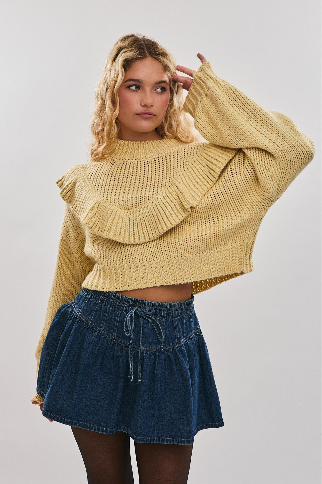 Woman wearing a yellow knitted sweater and blue denim shorts on a plain background available at Erin Rose Boutique.