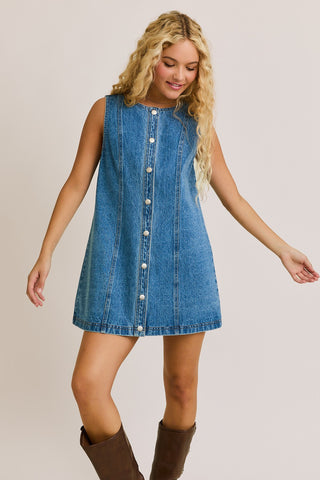Woman wearing a denim dress with buttons on a plain background