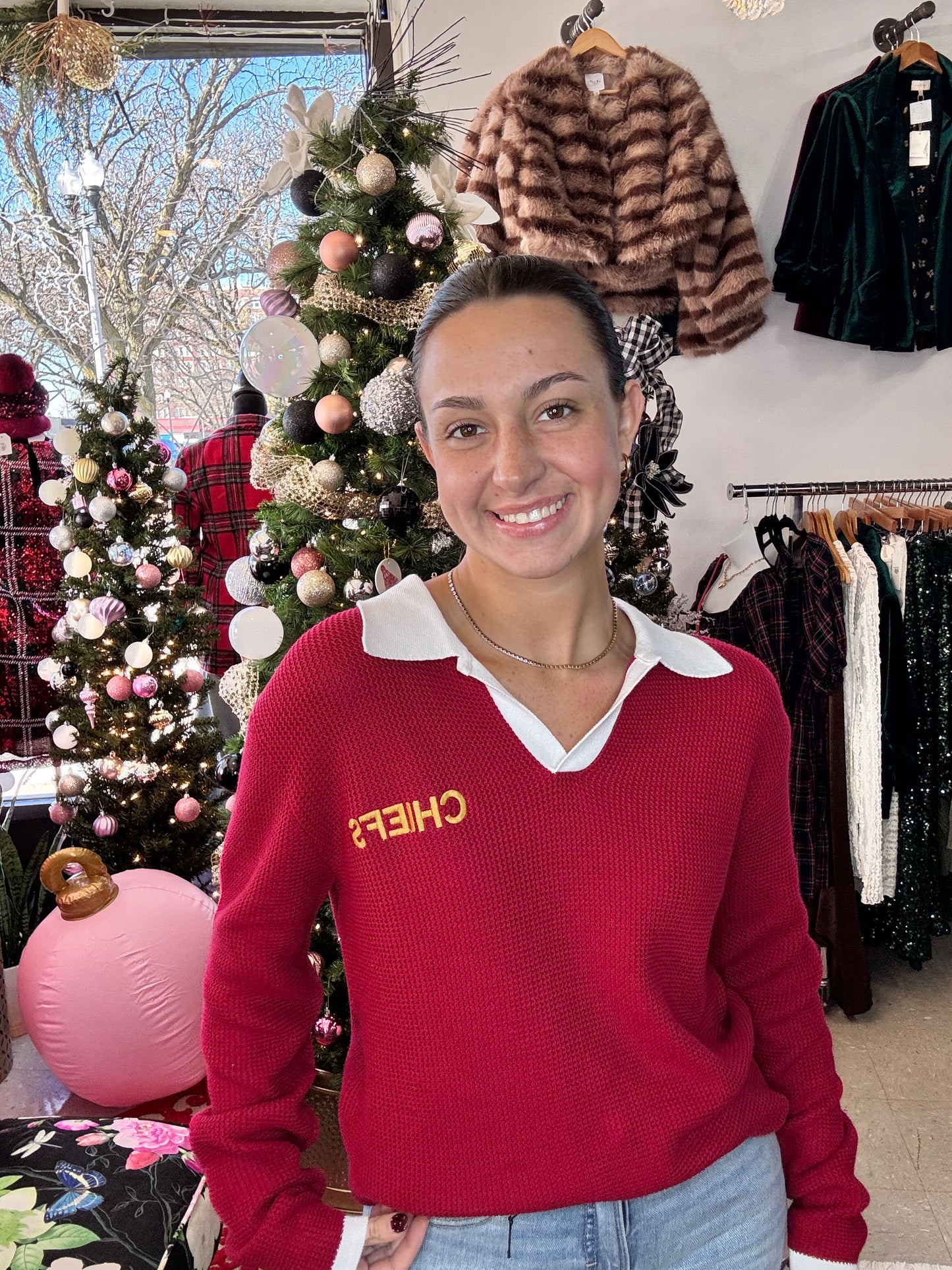 Person wearing a red sweater with 'CHIEFS' text, standing in front of Christmas decorations.