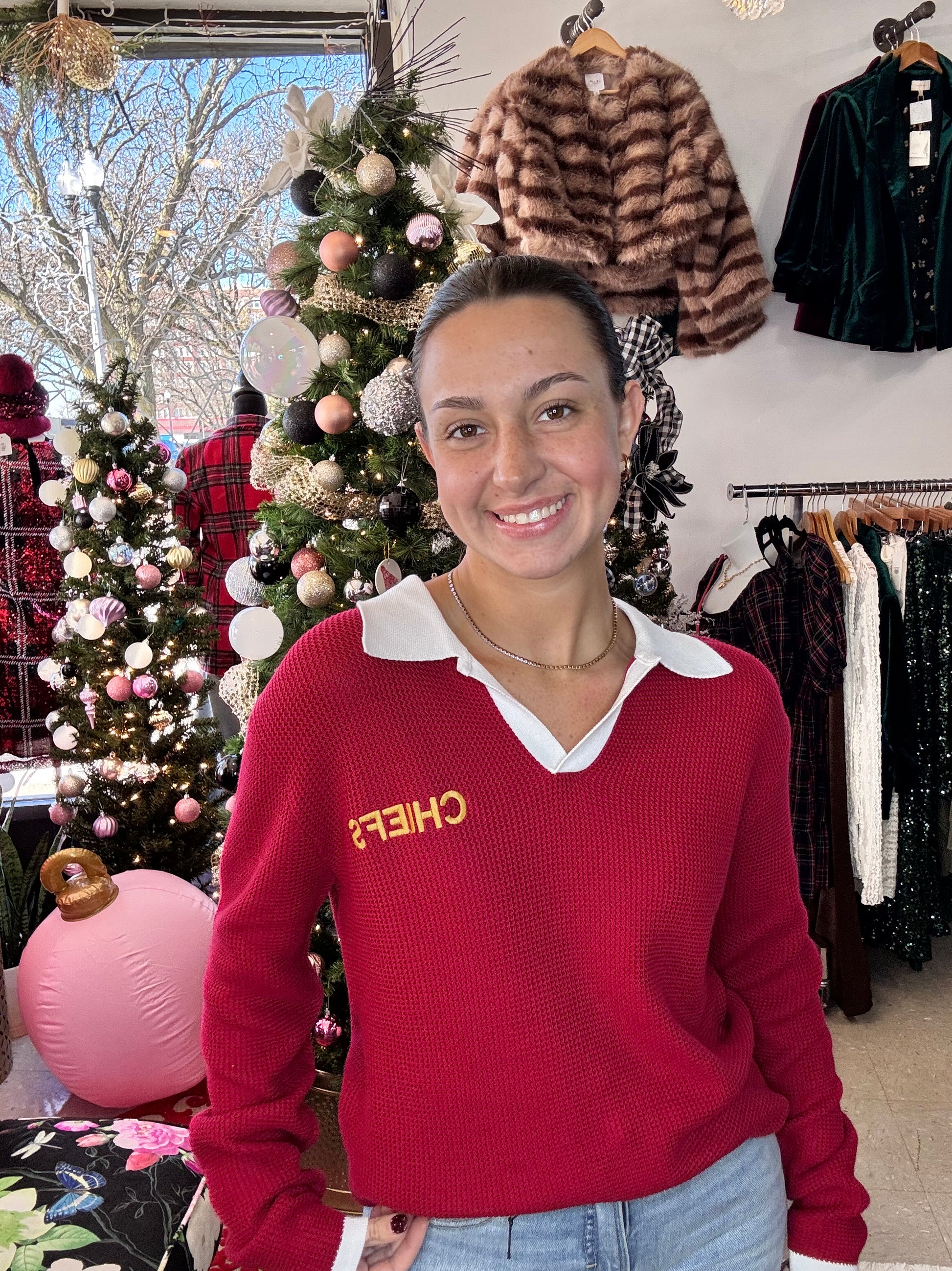 Person wearing a red sweater with 'CHIEFS' text, standing in front of Christmas decorations.