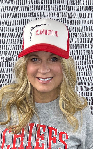 Person wearing a Kansas City Chiefs sweatshirt and cap against a patterned wall.