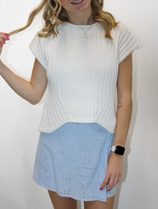 Model wearing a cream ribbed cap sleeve knit top styled with a light blue eyelet mini skirt.