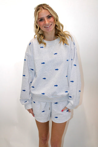 Model wearing a light gray sweatshirt and matching shorts lounge set with small blue fish print and drawstring waistband.