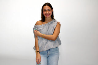 Model wearing a blue and white gingham one-shoulder top with tie detail, styled with light wash jeans.