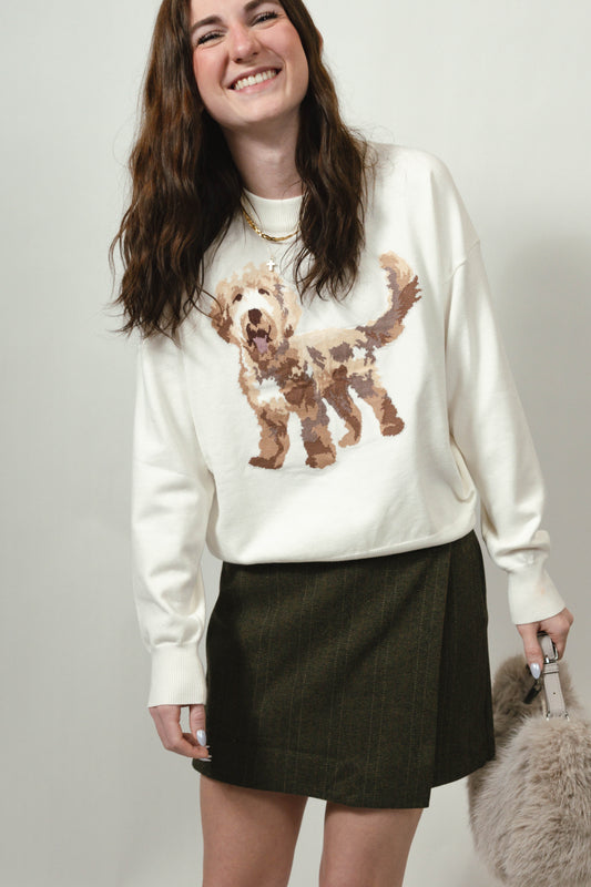 Person wearing a white sweater with a doodle puppy and a green skirt, holding a faux fur handbag