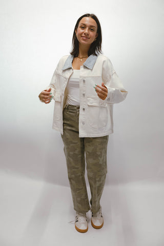 Woman wearing a cream utility jacket with light denim contrast collar styled with camo pants and white sneakers.