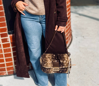Woman standing with striped denim and faux suede chocolate trench coat holding a faux fur fawn brown baguette shoulder bag