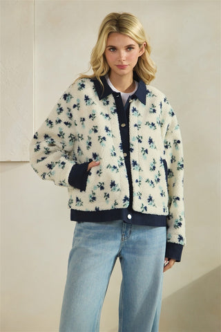 Woman wearing a floral-patterned jacket with navy accents and light blue jeans against a neutral background