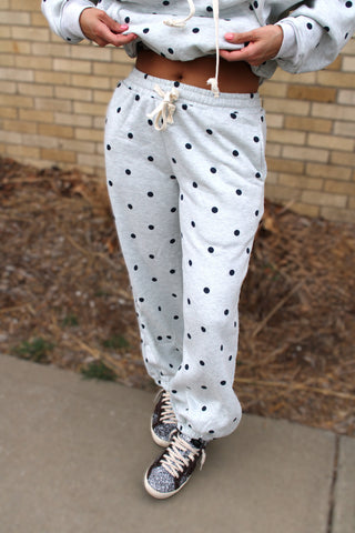 Person wearing a gray sweatshirt and heather grey with navy polka dot pants with sneakers on a sidewalk.